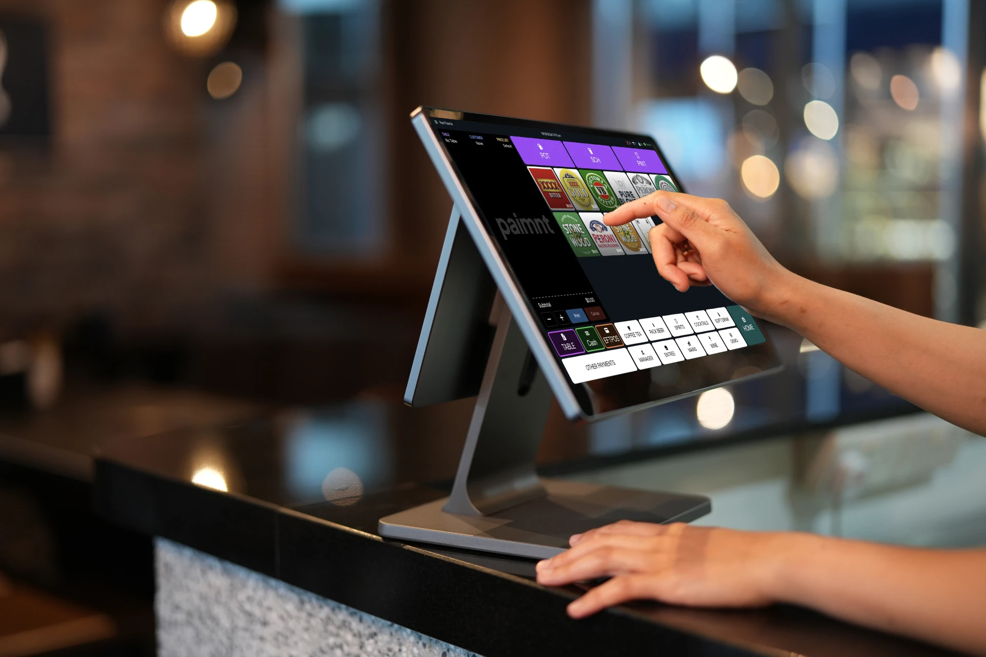 POS system on a shop counter with a shop assistants hands visible tapping the screen.