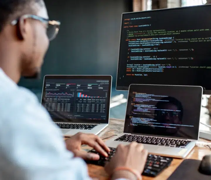 Developer working at a desk with two laptops and a desktop screen.
